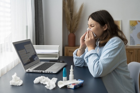 woman blowing nose at desk